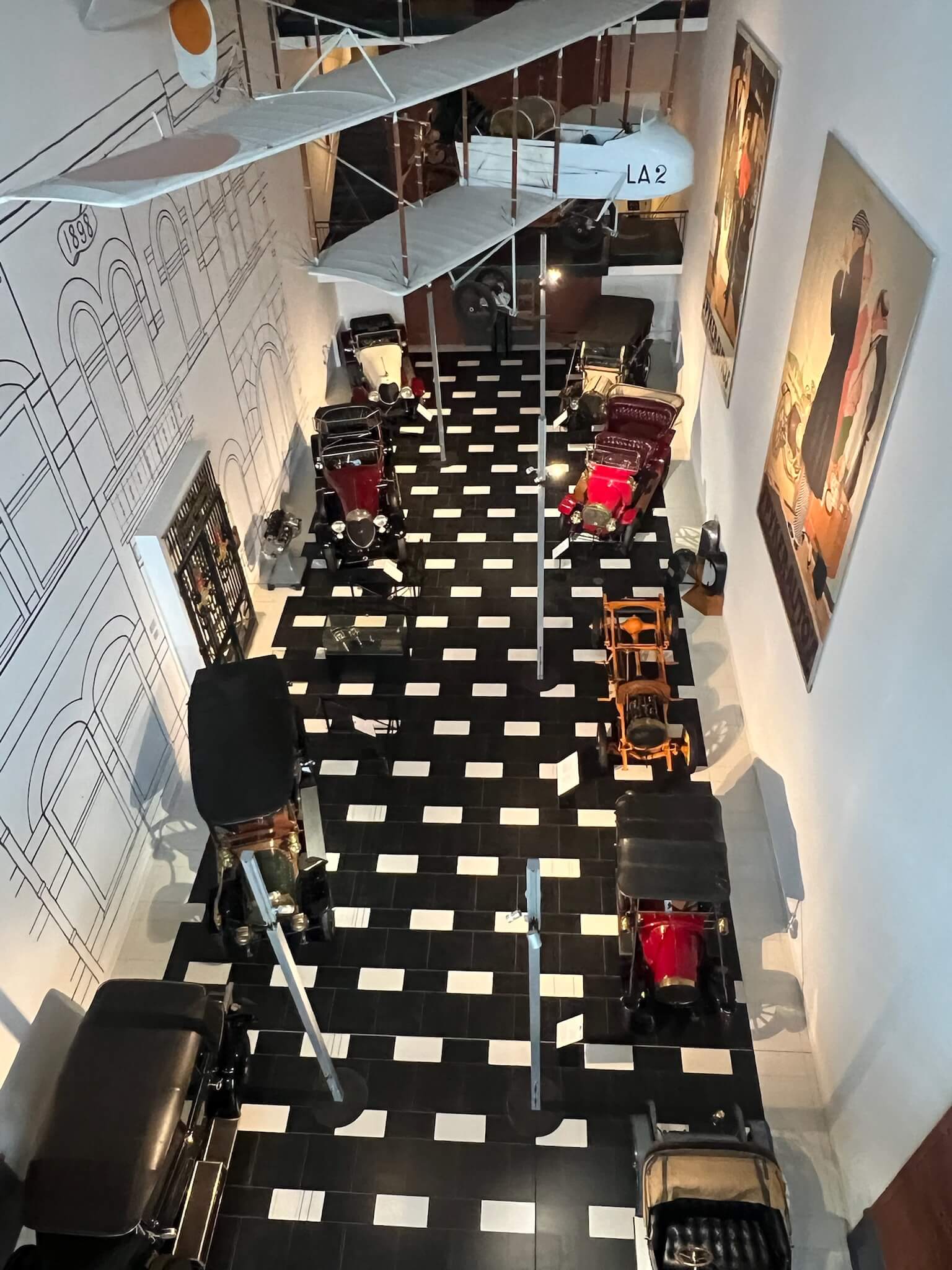 General view inside the Louwman Museum showing a multi-level gallery with vintage cars below and a suspended early aircraft overhead