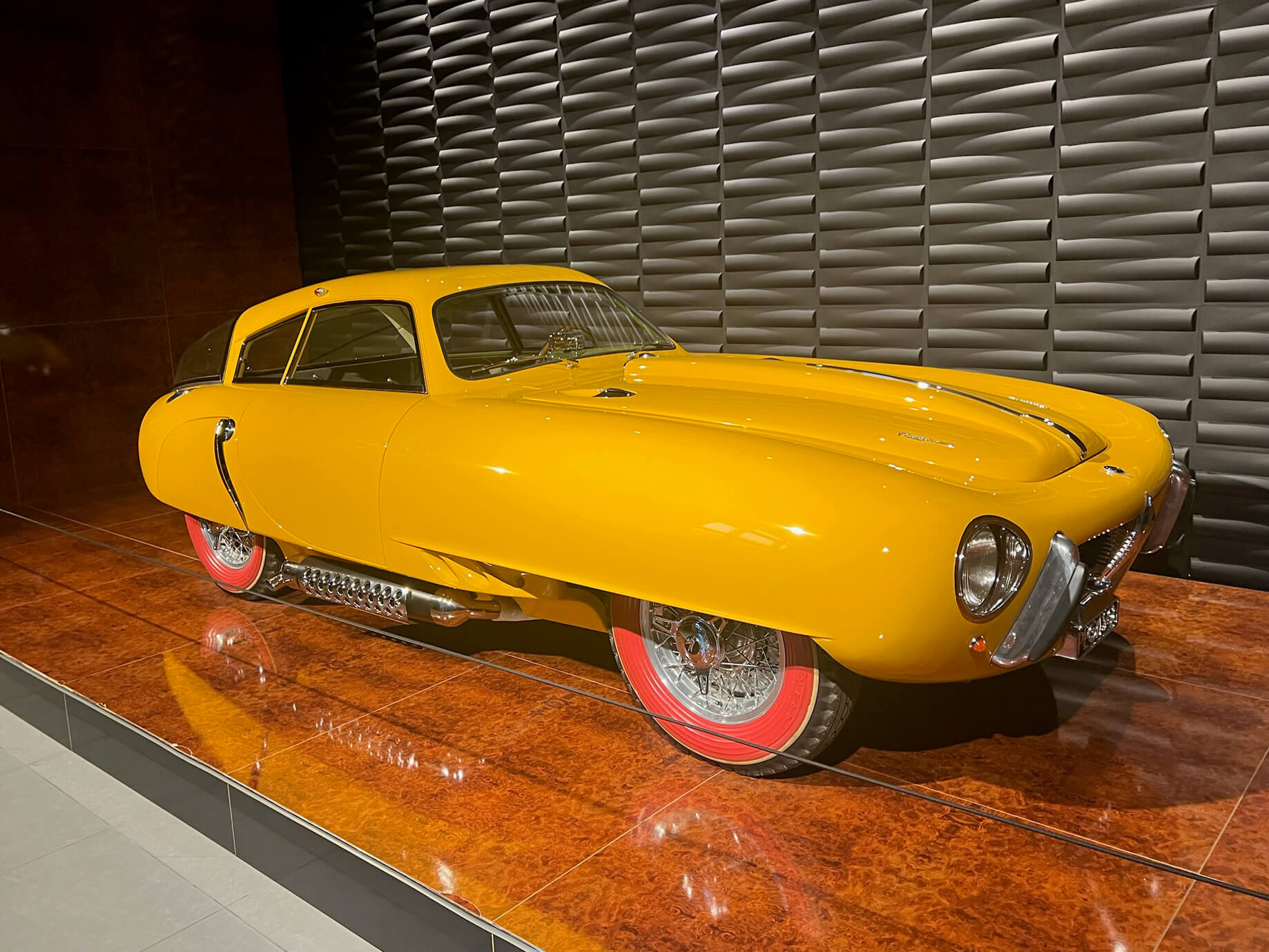 Bright yellow Pegaso Z-102 Cupula displayed at the Louwman Museum, photographed in a modern gallery setting with red wheels and chrome details